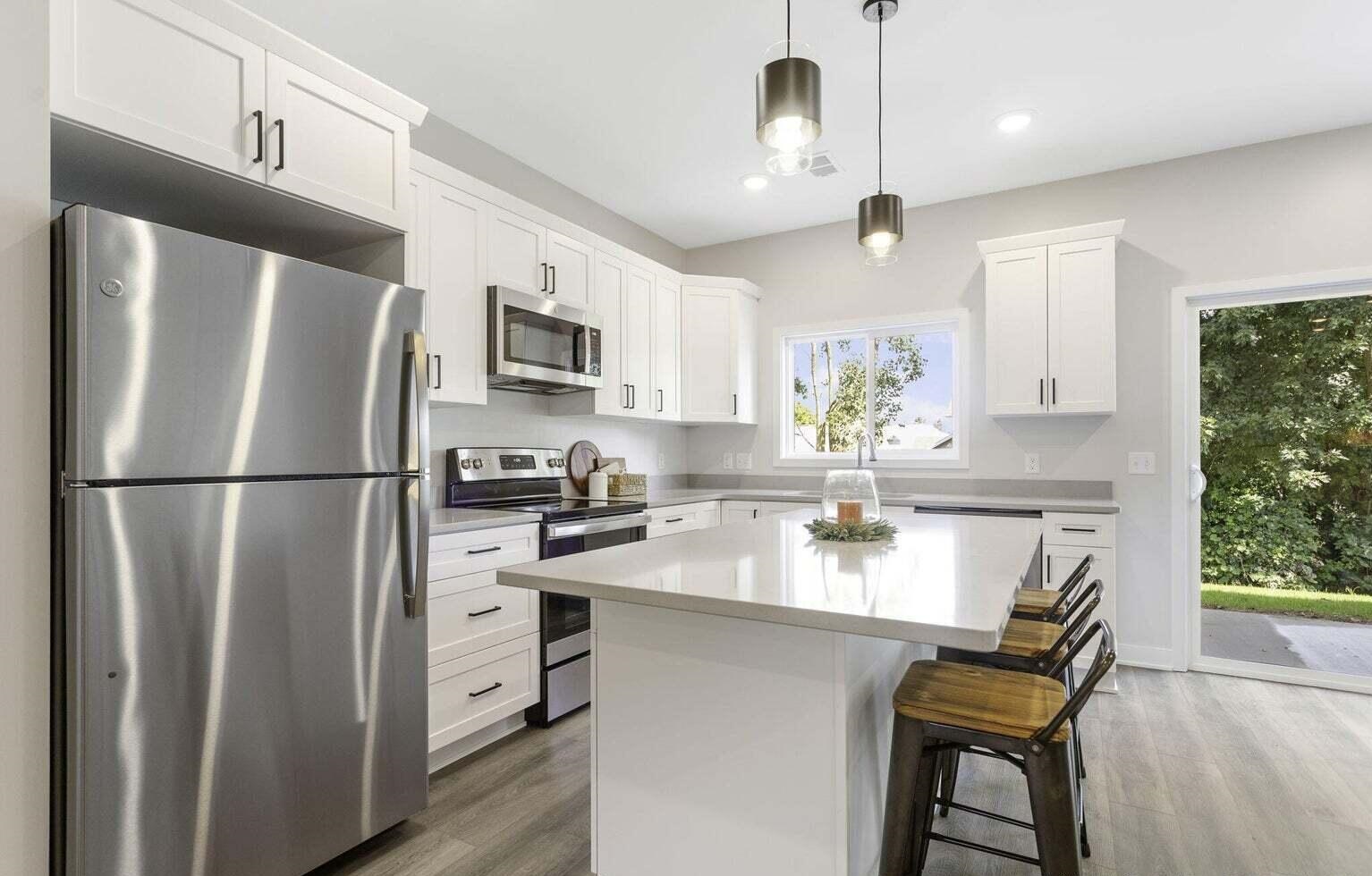 Modern white kitchen at Signature Estates featuring stainless steel appliances, shaker cabinets and a large center island